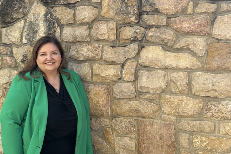 Marnie Wright is standing in front of a greystone wall on the USask campus