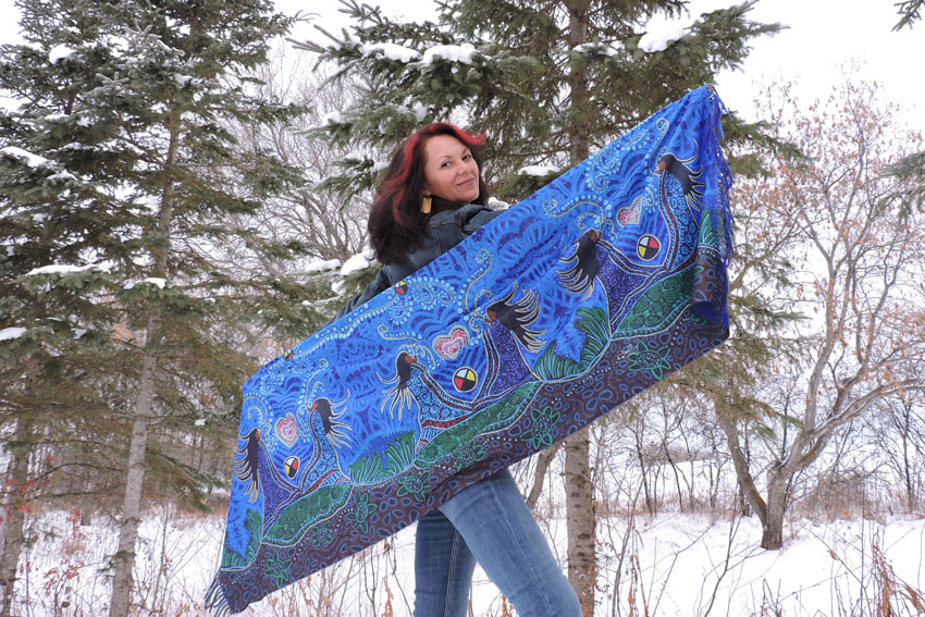 Leah Dorion is standing outside in the snow holding up a colourful blue scarf behind her.