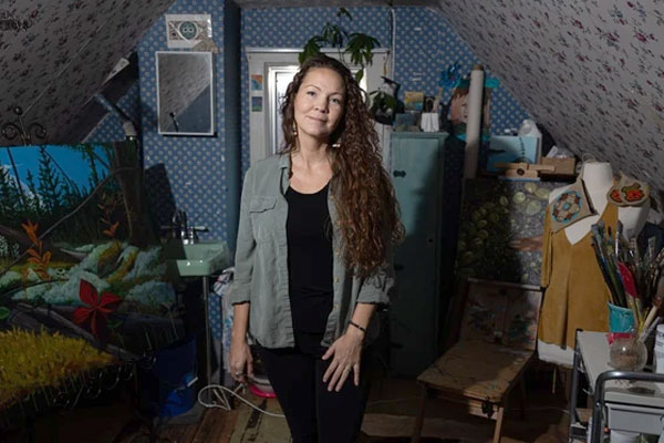 Vanessa Hyggen is standing in her home studio space surrounded by her artwork