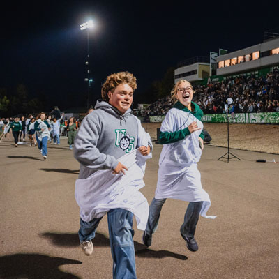 2 USask students in the toga run with a crowd in the background